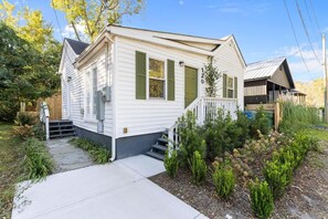 A single-story mobile home with a front porch, a small set of steps, and a garden area with various plants.