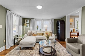 A living room with a sofa, ottoman, coffee table, and a vase with flowers.