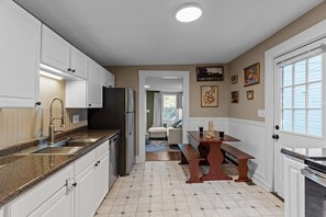 A kitchen with white cabinets, a granite countertop, a refrigerator, and a dining area with a wooden table and bench.