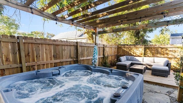 A hot tub under a wooden pergola, surrounded by a wooden fence, with outdoor furniture and a stone pathway. - Jasmine Cottage - Hot Tub - Very Pet Friendly (Wilmington)