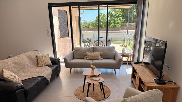 Un salon moderne avec un canapé, un fauteuil et un téléviseur posé sur un meuble en bois.