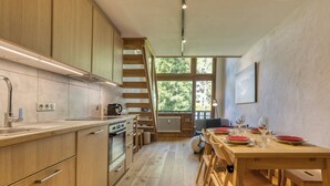 A modern kitchen with wooden cabinets, a built-in oven, and a dining area with a wooden table and chairs. - Brévent Loft – Cozy 3-bedroom duplex, 250m to Planpraz cable car (Chamonix-Mont-Blanc)