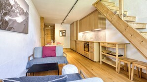 A modern interior with a wooden staircase, a dining area with a table set for two, and a kitchen with wooden cabinets and appliances. - Brévent Loft – Cozy 3-bedroom duplex, 250m to Planpraz cable car (Chamonix-Mont-Blanc)