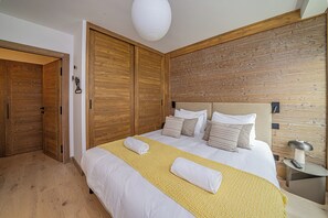 A bedroom with a wooden headboard, a bed with white bedding and multiple pillows, a bedside table with a lamp, and a wooden wardrobe.