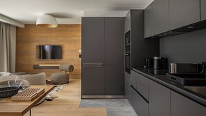 Een moderne keuken met donkere kastjes, een flatscreen televisie bevestigd aan een houten wand, en een eethoek met een houten tafel en stoelen.