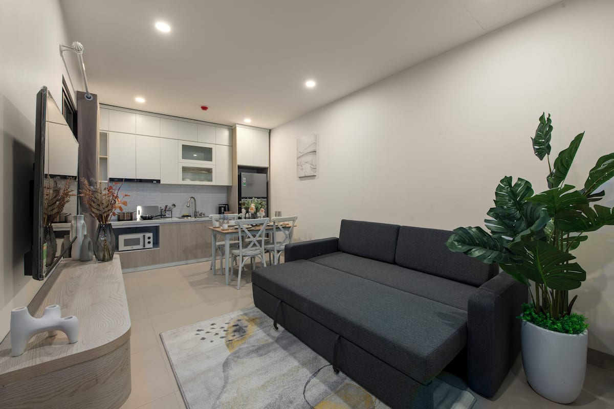 Uma sala de estar moderna com um sofá cinzento, uma mesa lateral de madeira e uma grande planta em vaso.