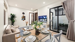 Un espace repas moderne avec une table en bois dressée pour quatre personnes, un canapé et un téléviseur en arrière-plan.