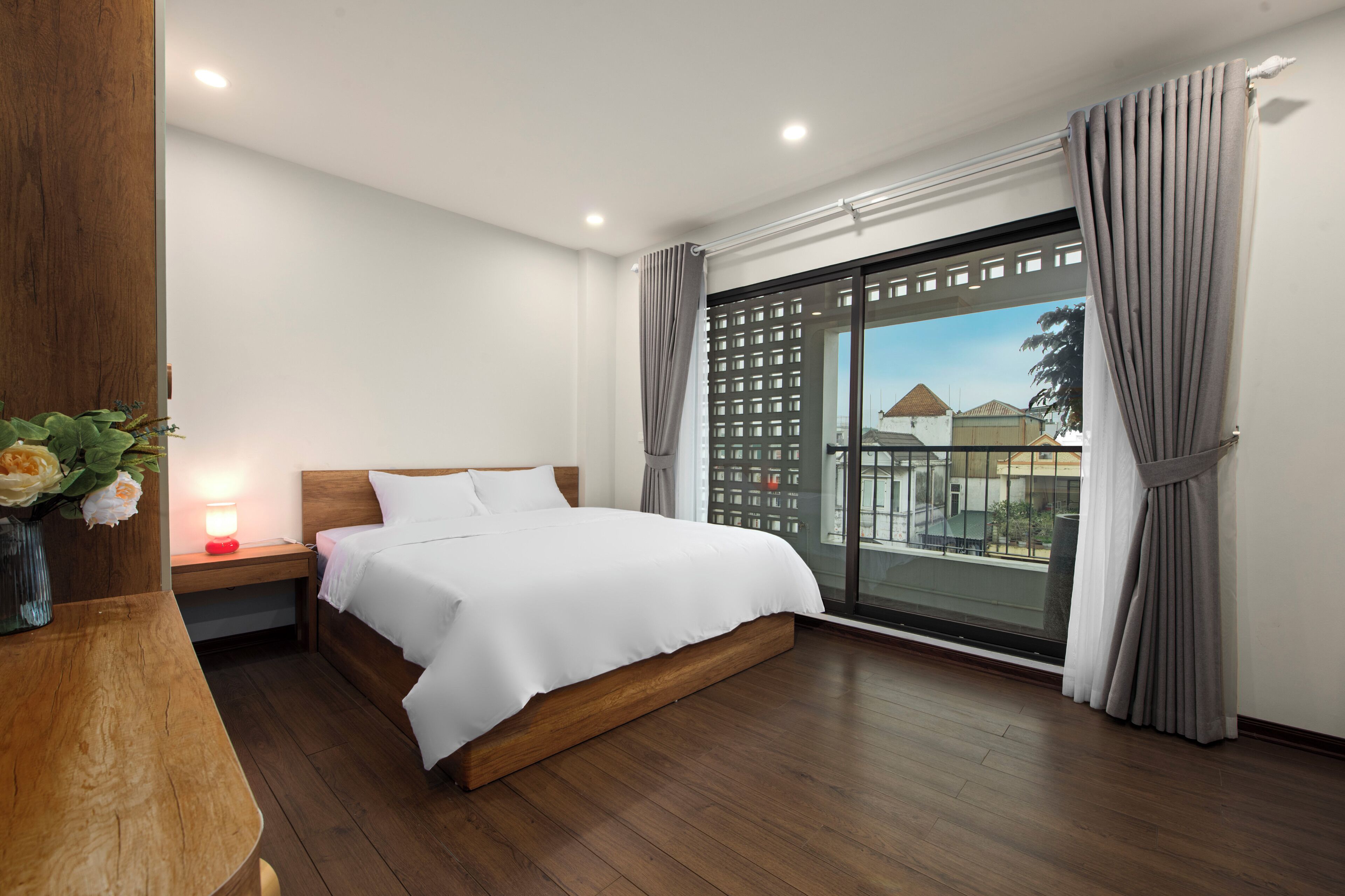 A bedroom with a wooden bed, a nightstand, a bedside table with a lamp, and a view through a sliding glass door.