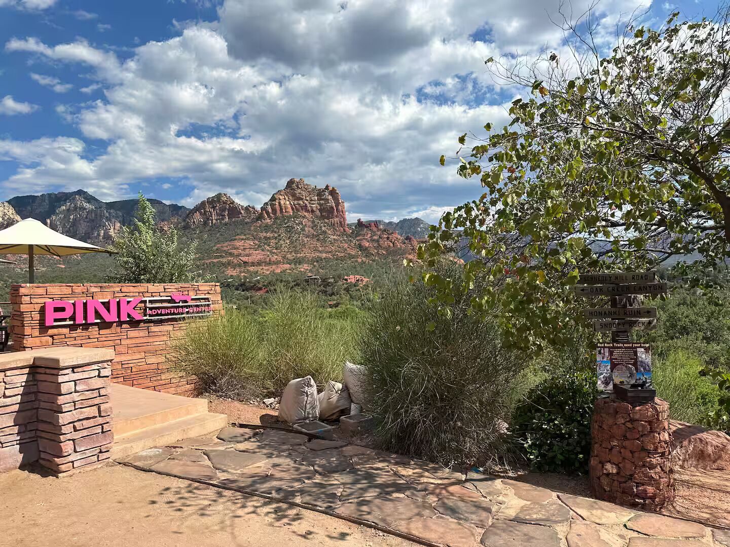 Señal del parque Pink Adventure Park con vista a formaciones rocosas rojas al fondo.