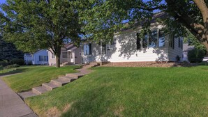 A two-story house with a front yard, a sidewalk, and a tree providing shade.