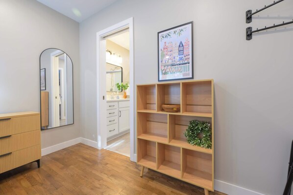 A hallway with a wooden dresser, a mirror, a framed picture, and a wooden shelf unit. - The Mid-Town Cottage (Pella)