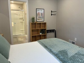 A bedroom with a bed, a wooden shelf, a framed picture, and a shower. - The Mid-Town Cottage (Pella)
