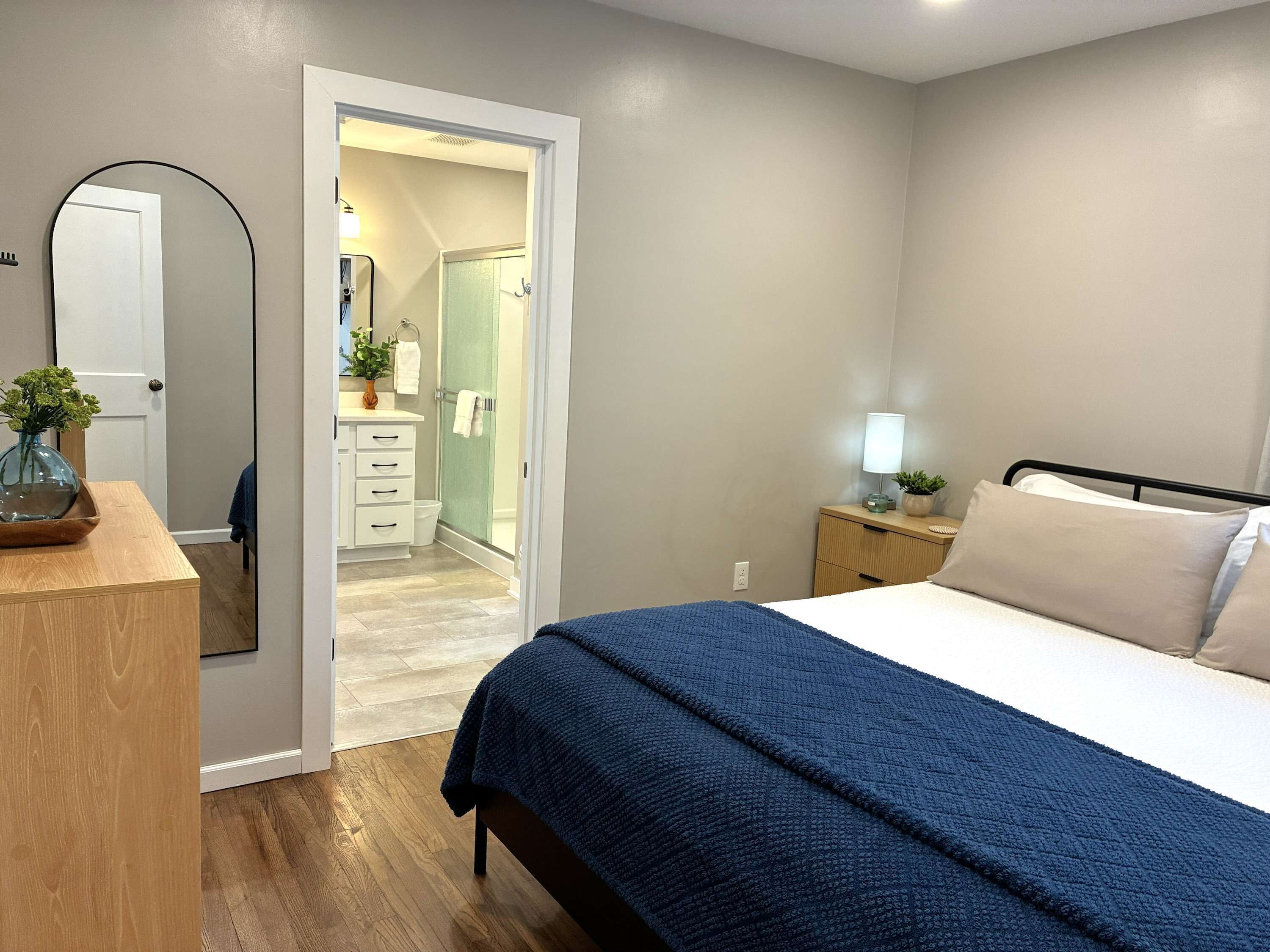 A bedroom with a bed, bedside table, lamp, and a mirror.