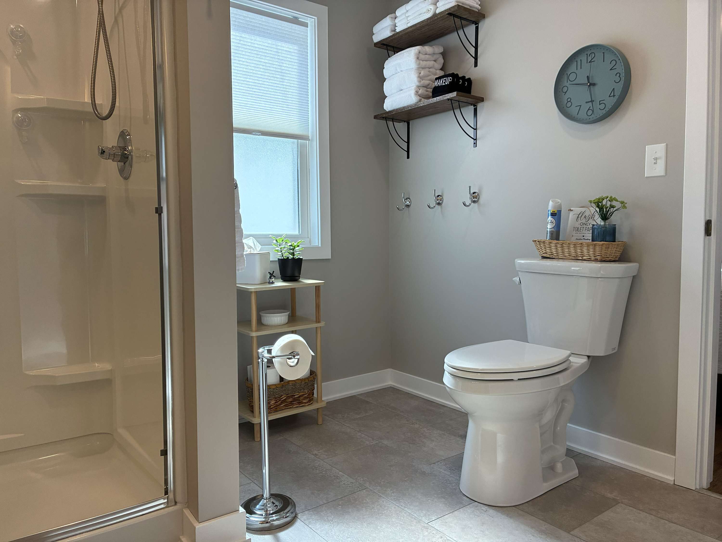 A bathroom with a shower, toilet, and shelves with towels.