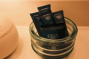 A glass bowl containing several packets labeled 'Marula Soul' and a white bath sponge. - The Mid-Town Cottage (Pella)
