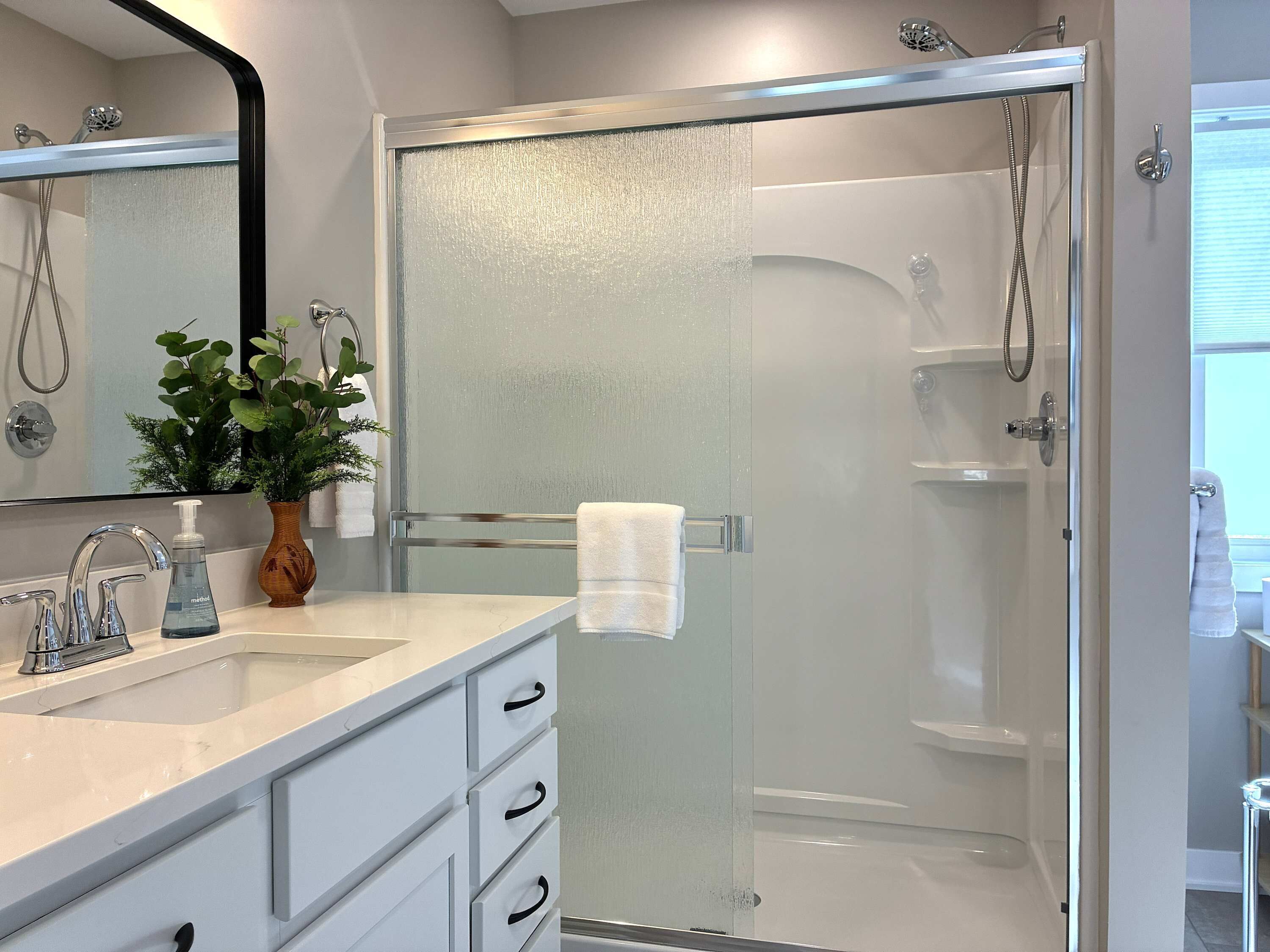 Un baño moderno con ducha de vidrio, un lavamanos blanco con dispensador de jabón y un espejo sobre el lavamanos.