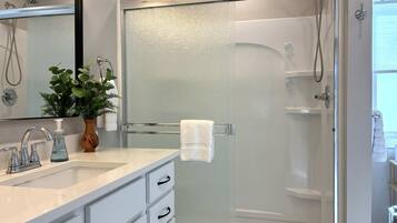Un baño moderno con ducha de vidrio, un lavamanos blanco con dispensador de jabón y un espejo sobre el lavamanos.