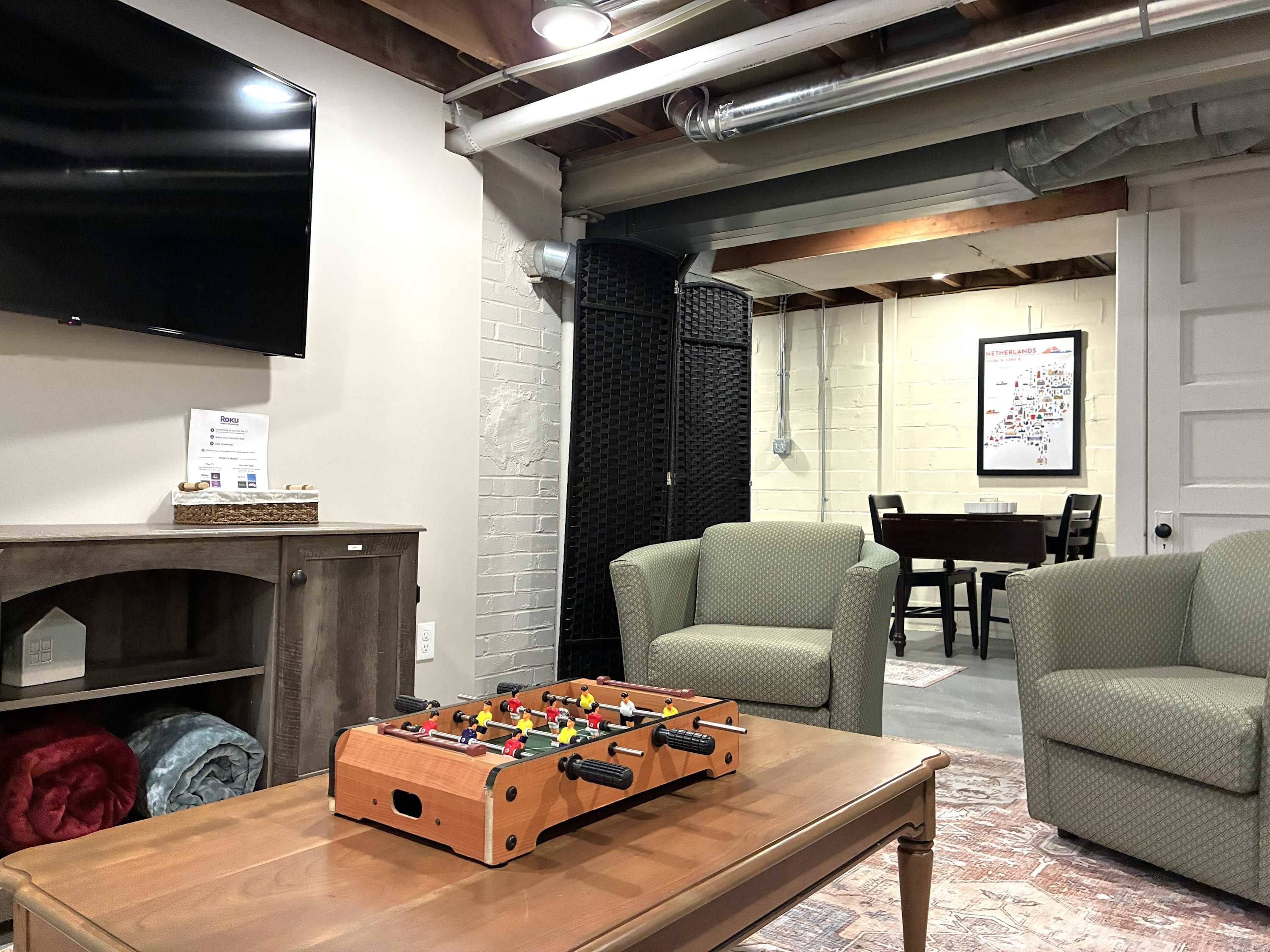 A cozy living room with a foosball table, a flat-screen TV, and a brick wall.