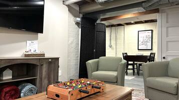 A cozy living room with a foosball table, a flat-screen TV, and a brick wall.