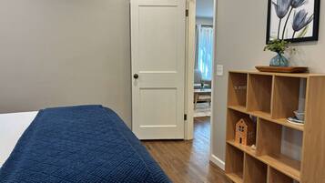 Ein Schlafzimmer mit einem Bett, einer Tür, einem Holzregal mit Dekoration und einem gerahmten Bild an der Wand.