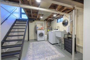 A laundry room with a washing machine, dryer, sink, and a small staircase. - The Mid-Town Cottage (Pella)