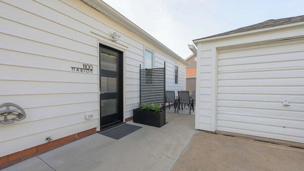 A building with a garage door, a door with a black frame, and a small outdoor seating area with chairs and a table.