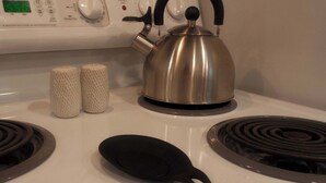 A stove with a kettle, two salt shakers, and a black pan.