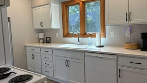 A kitchen with white cabinets, a stove, a sink, and a window with wooden frames.