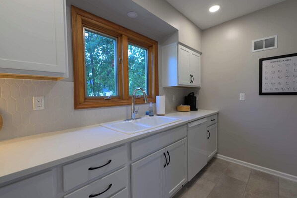 A modern kitchen with a large window, white cabinets, and a calendar on the wall. - The Mid-Town Cottage (Pella)