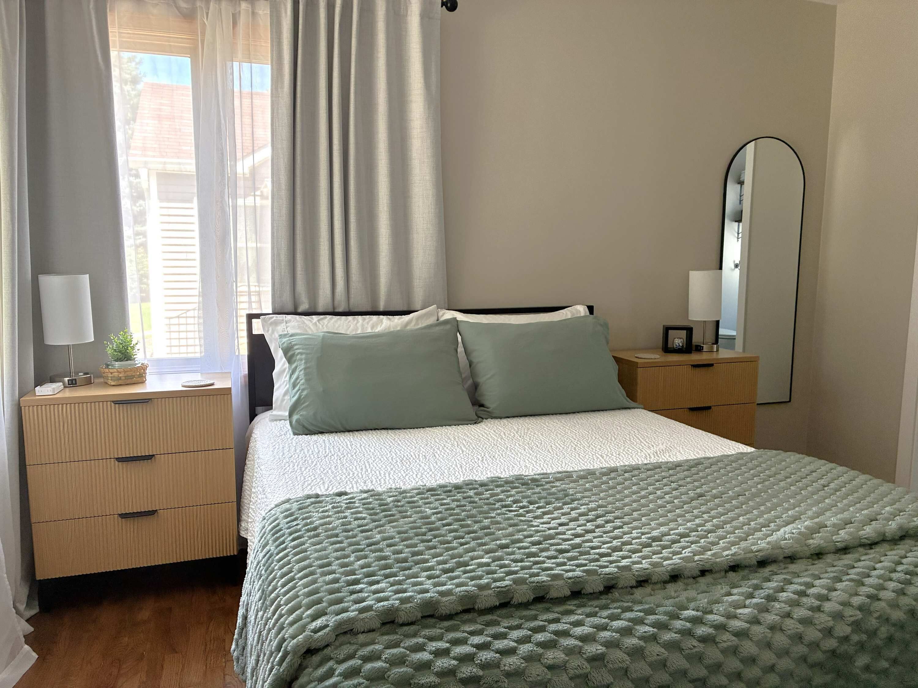 Een slaapkamer met een bed, nachtkastjes, een spiegel en een raam met gordijnen.