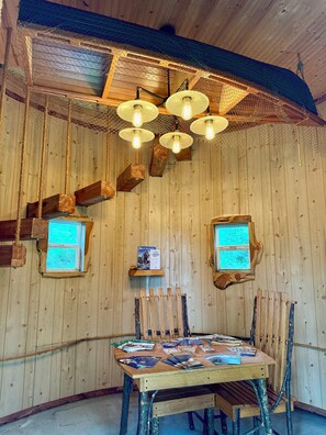 Ein rustikales Zimmer mit Holzboden, einem Holztisch, Stühlen und hängenden Leuchten.