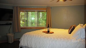 Une chambre à coucher avec un lit, un ventilateur de plafond, une fenêtre avec des rideaux et une bouteille de vin posée sur le lit.