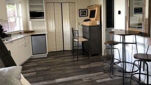 Une cuisine compacte avec des meubles blancs, un four à micro-ondes encastré et une table à manger en bois, accompagnée de tabourets.