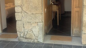 A stone wall leading to a bathroom with a mirror, wooden door, and tiled floor. - Guest room 25m2 (Figari)