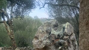 A large rock formation with a small wooden structure on top, surrounded by trees and a stone wall. - Guest room 25m2 (Figari)
