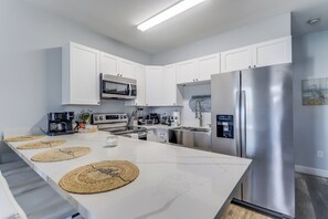 A modern kitchen with white cabinets, stainless steel appliances, and a central island with woven placemats.