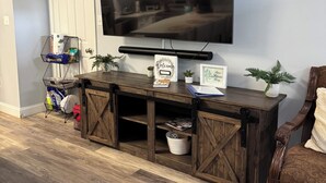 Ein Wohnzimmer mit an der Wand montiertem Fernseher, einer Holzunterhaltungsecke darunter, einer Tür und einem Blumentopf.