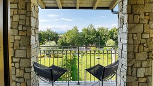A balcony with stone walls and a view of a grassy area with trees.