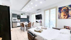 A modern hotel room with a bed, a desk, and a kitchenette.