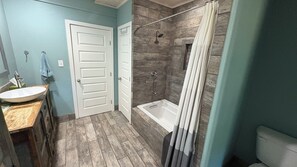 A bathroom with a wooden vanity, a bathtub, and a shower area. - Lake Cottage 200 yards from the Lake Texoma shoreline! (Pottsboro)