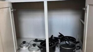 Una cucina con un piano di lavoro bianco e due pensili contenenti pentole e padelle.