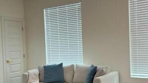 Un soggiorno con un divano beige, due cuscini, un tavolino e una ventola a soffitto.