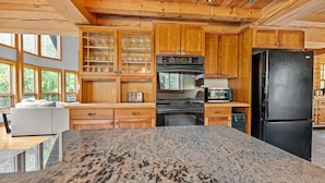 A modern kitchen with granite countertops, wooden cabinets, a black refrigerator, and a built-in oven.
