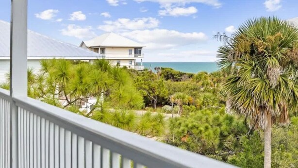 A coastal property with a view of the ocean, a white building, and dense greenery.