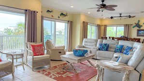 A living room with a white leather sofa, a white wicker chair, a round coffee table, and a red rug.