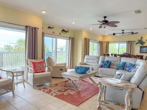 A living room with a white leather sofa, a white wicker chair, a round coffee table, and a red rug.