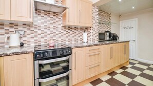 A kitchen with wooden cabinets, a black stove, a microwave, and a tiled backsplash. - Spacious 3 Bed 2 Baths Free WiFi Central Location (MIDDLESBROUGH)