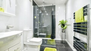 A modern bathroom with a glass-enclosed shower, a white toilet, a sink with a mirror, and a towel rack with a green towel. - Spacious 3 Bed 2 Baths Free WiFi Central Location (MIDDLESBROUGH)