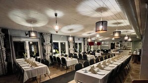 Un restaurant doté de nombreuses tables dressées pour le service, où l’éclairage est assuré par un mélange de sources naturelles et artificielles.
