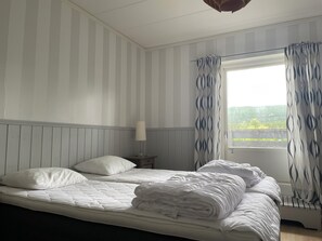 Een slaapkamer met een bed, nachtkastje, lamp en raam met gordijnen.